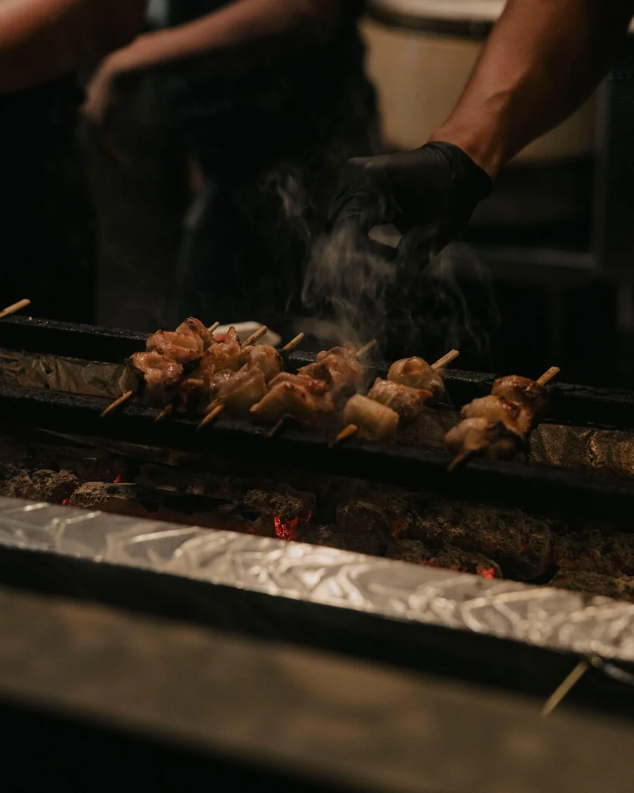 Kömür ocağında tavuk yakitori şişleri; duman yükseliyor.