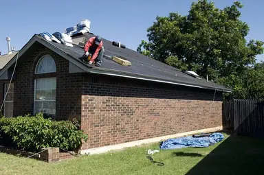 Roofer replacing shingles on a brick house