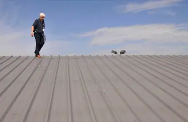 Inspector walking a hail-damaged metal roof